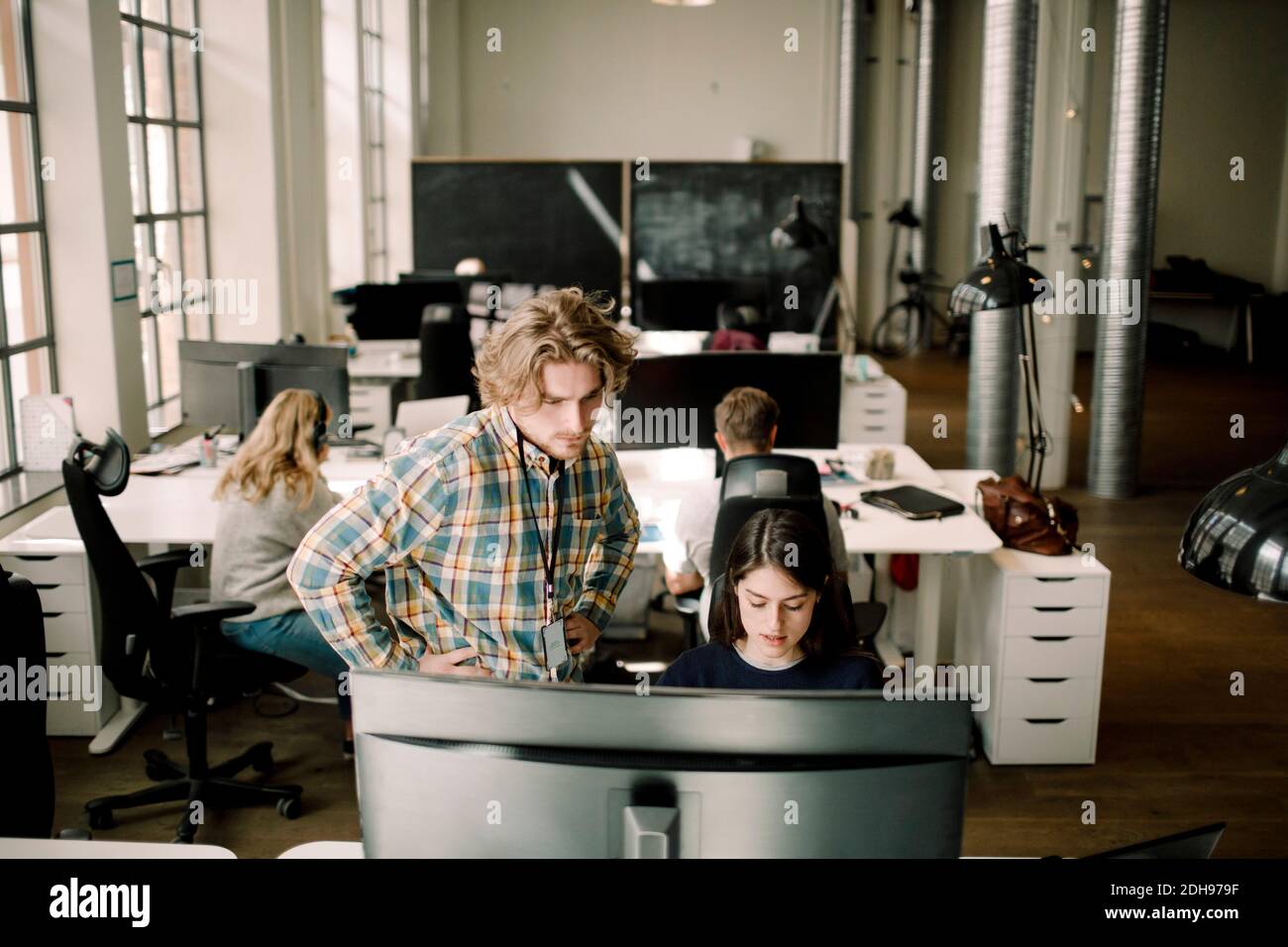 Ein Geschäftsmann schaut auf den Computer, während eine Kollegin im Büro sitzt Stockfoto