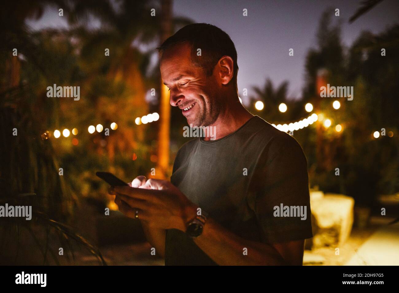 Lächelnder Mann, der während des Sonnenuntergangs mit dem Telefon gegen den Himmel telefoniert Stockfoto