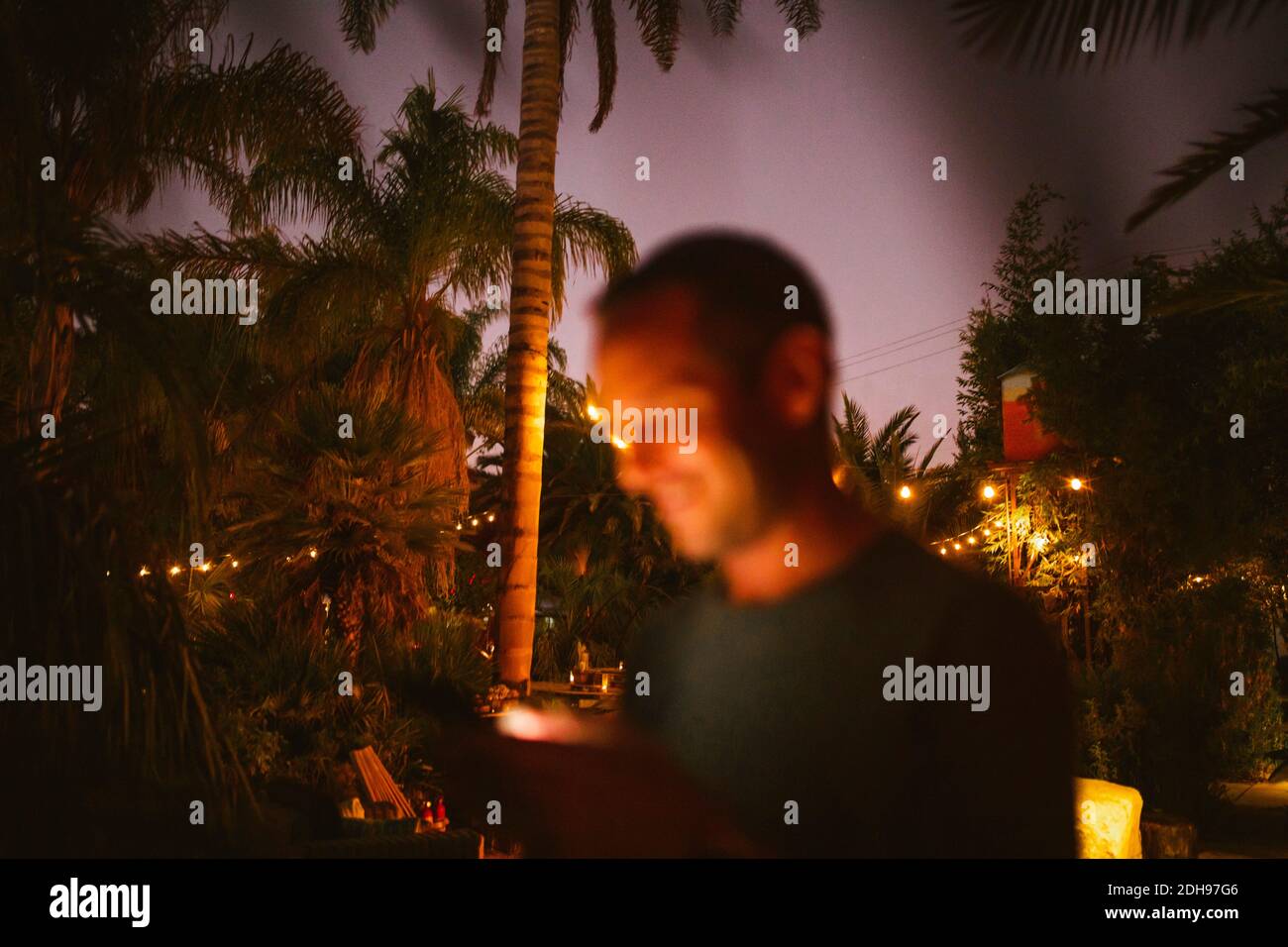 Lächelnder Mann, der während des Sonnenuntergangs mit dem Telefon gegen Bäume telefoniert Stockfoto