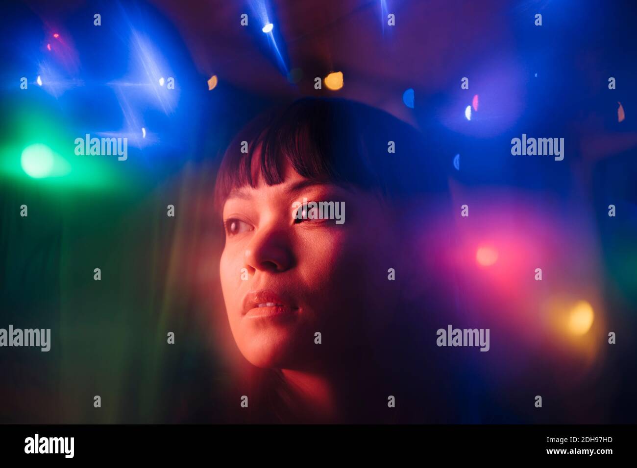 Nachdenkliche junge Frau, die inmitten von bunten Lichtern in sich hinschaut Restaurant Stockfoto