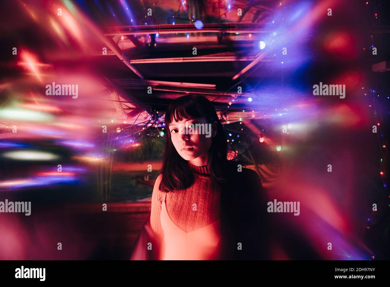 Porträt einer jungen Frau, die inmitten von beleuchteten bunten Lichtern steht An der Bar Stockfoto