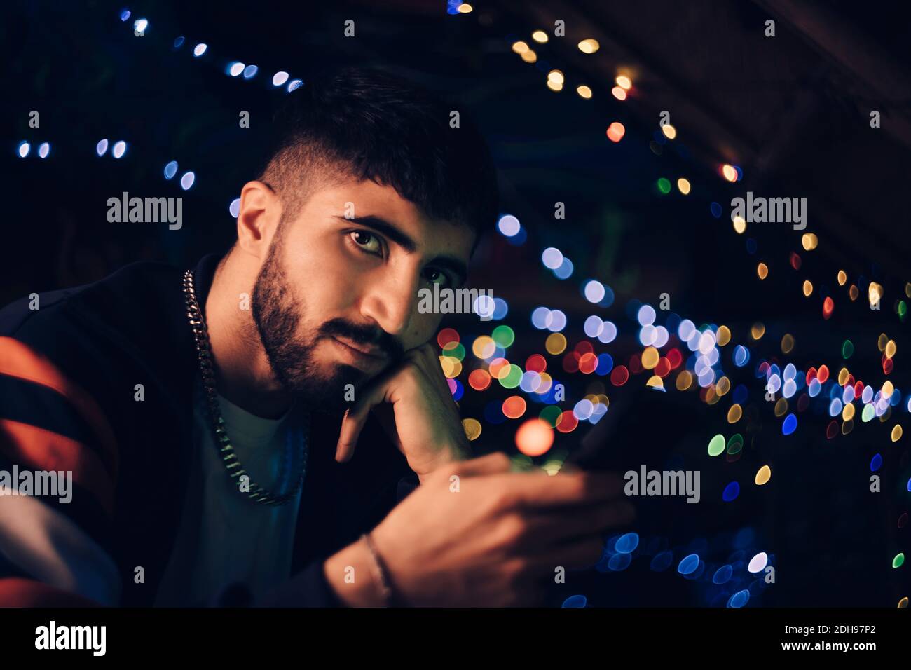 Porträt des jungen Mannes hält Smartphone gegen bunte Lichter An der Bar Stockfoto