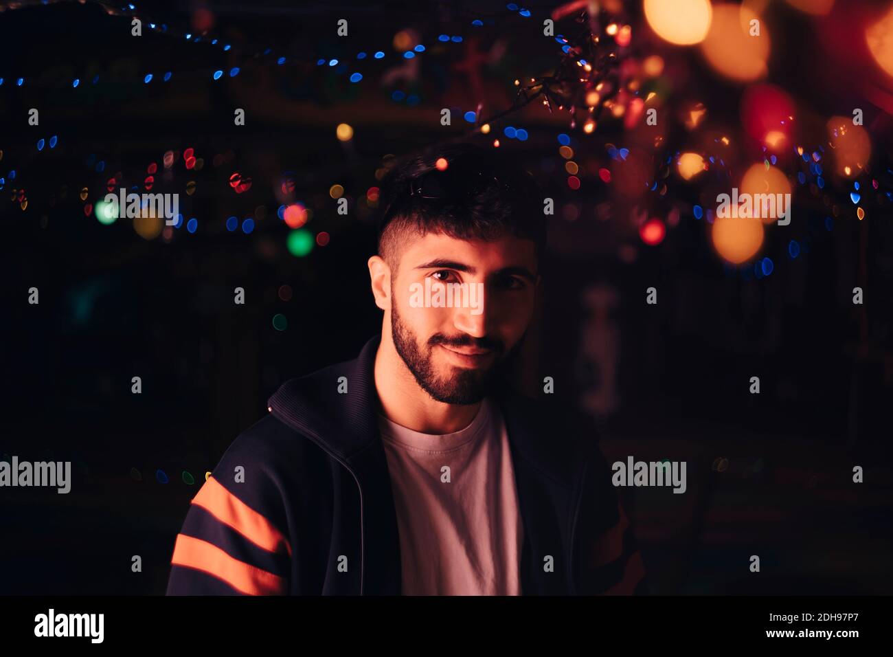 Porträt von lächelnden bärtigen Mann gegen beleuchtete bunte Lichter an Bar Stockfoto