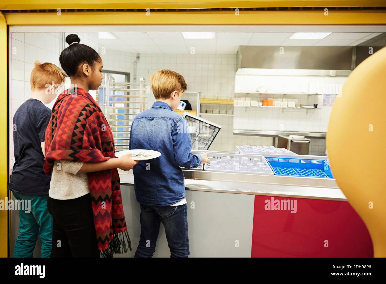 Die Schüler legen Teller in Kiste nach dem Mittagessen in der Schule Cafeteria Stockfoto