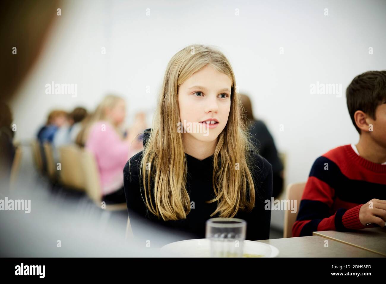 Nachdenkliches Mädchen, das während der Mittagspause in der Schule am Tisch sitzt Cafeteria Stockfoto