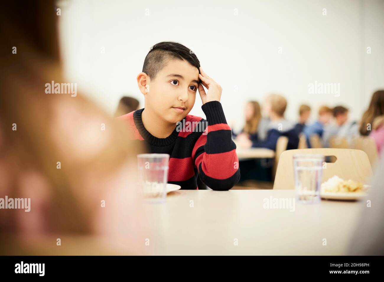 Nachdenklicher Junge, der während der Mittagspause in der Schule am Tisch sitzt Cafeteria Stockfoto