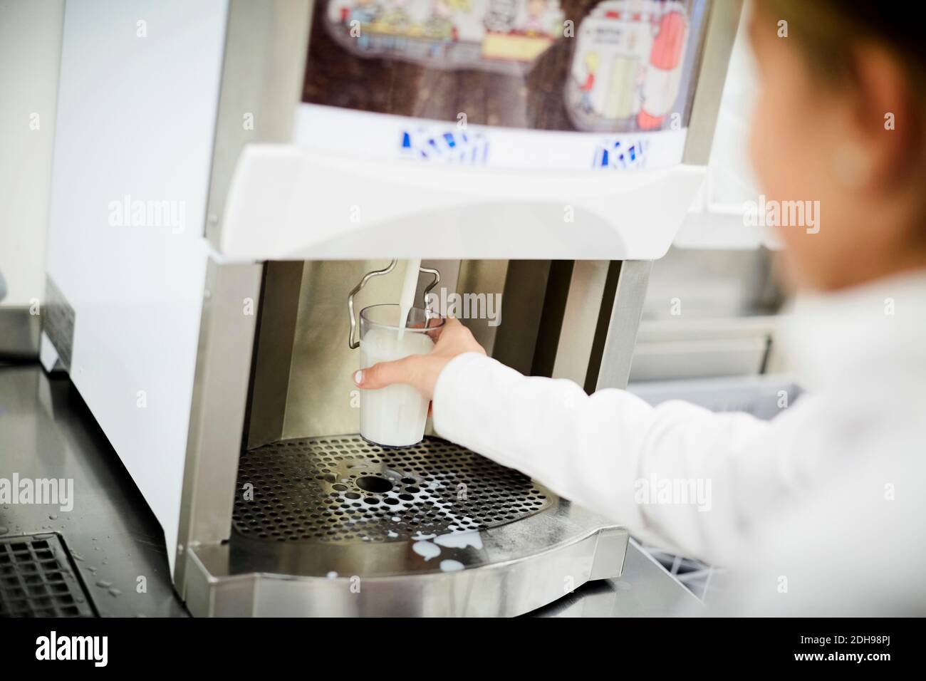 Schulmädchen Füllen Glas Milch aus der Maschine in der Schule Cafeteria Stockfoto