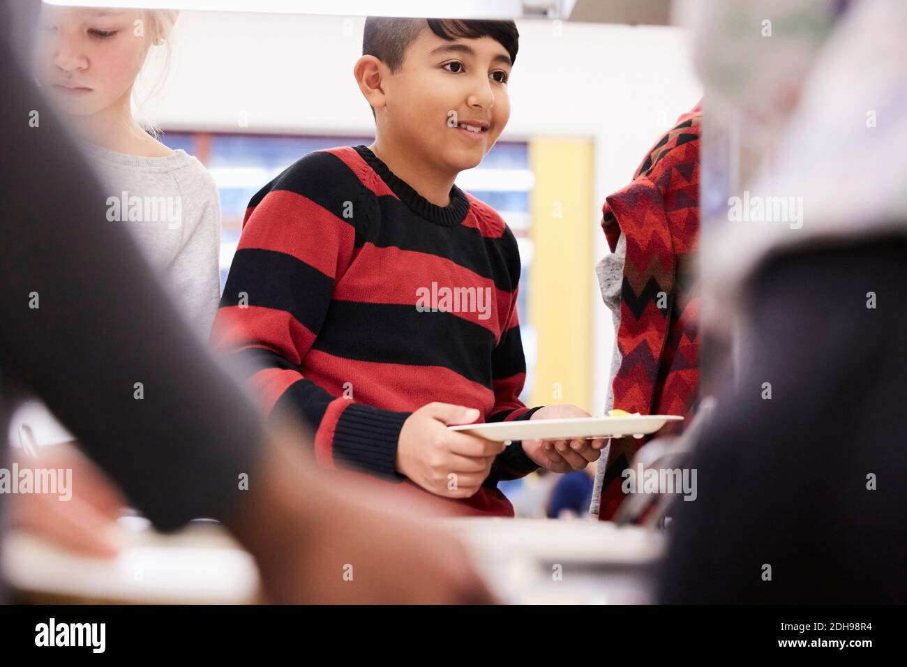 Junge hält Teller in der Mittagslinie in der Schulkantine Stockfoto