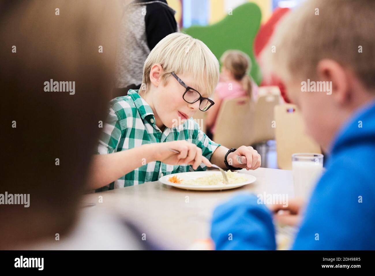 Junge, der in der Schulkantine am Tisch zu Mittag gegessen hat Stockfoto