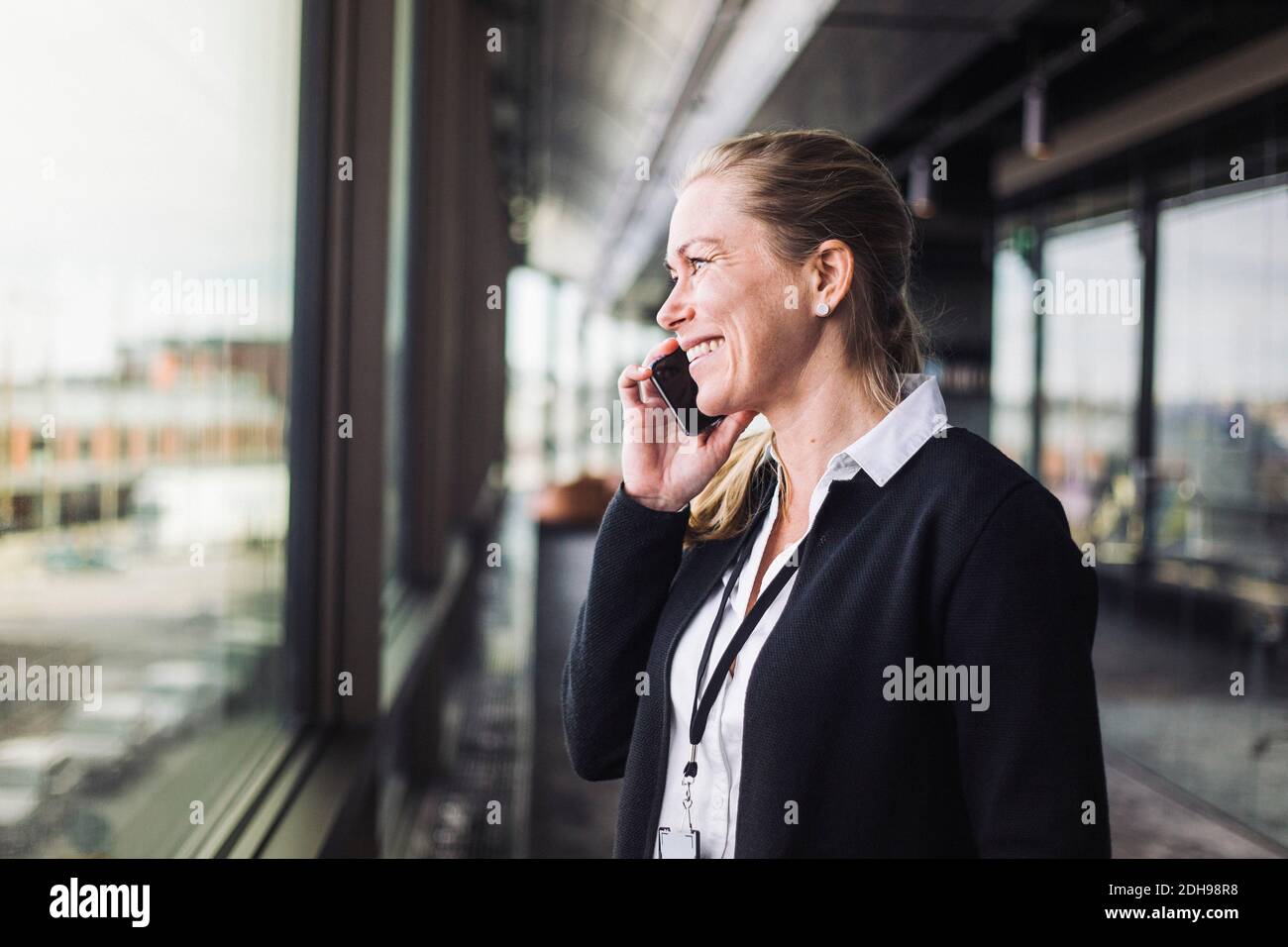 Lächelnder Unternehmer, der am Arbeitsplatz steht und mit dem Handy spricht Stockfoto