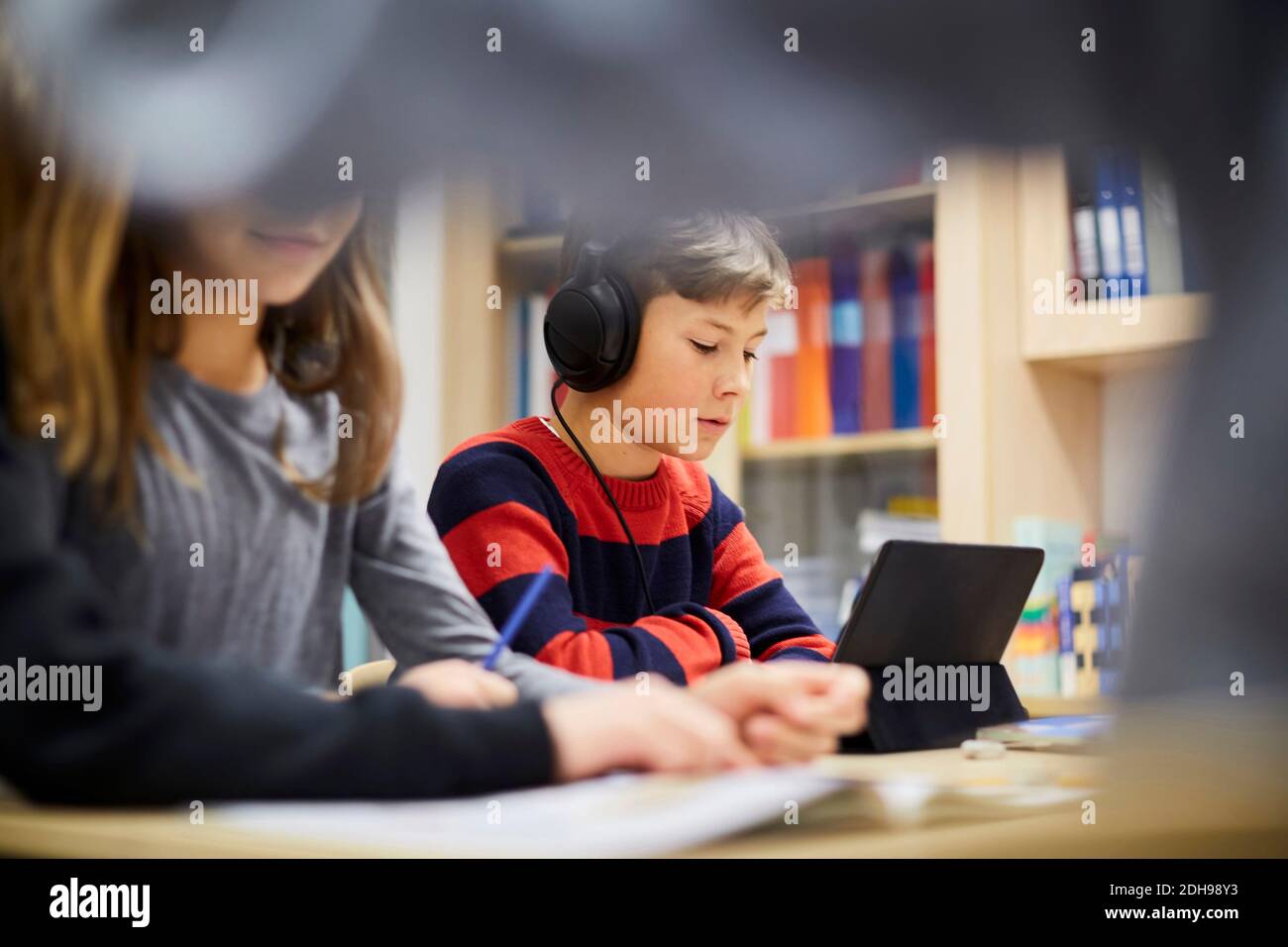 Junge, der Kopfhörer trägt, während er im Klassenzimmer auf ein digitales Tablet schaut Stockfoto