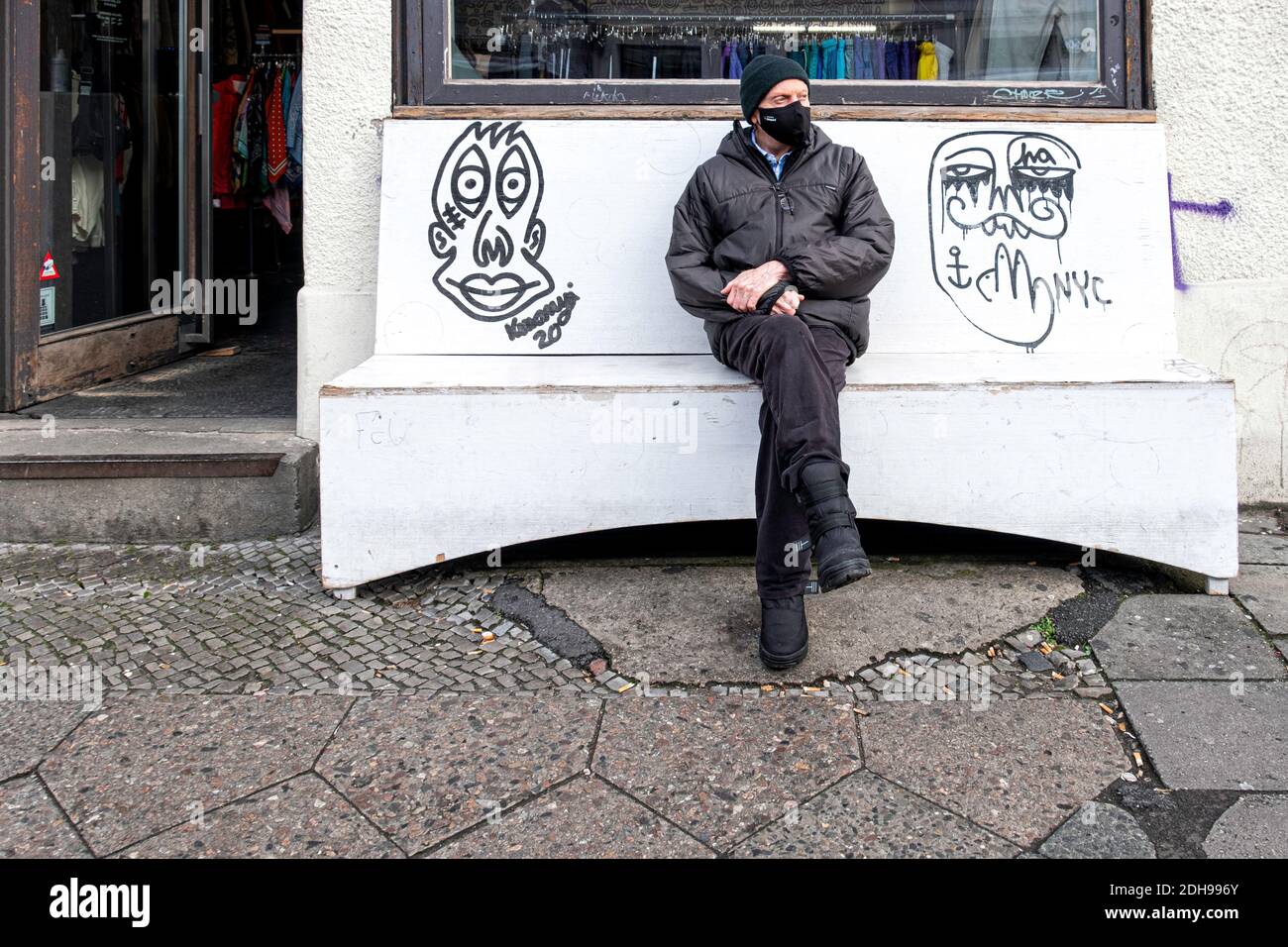 Ältere Haupt tragen Gesichtsmaske sitzt außerhalb Archiv Bekleidungsgeschäft während Corona Pandemie. Rosenthaler Strasse 72,Mitte,Berlin,Deutschland Stockfoto