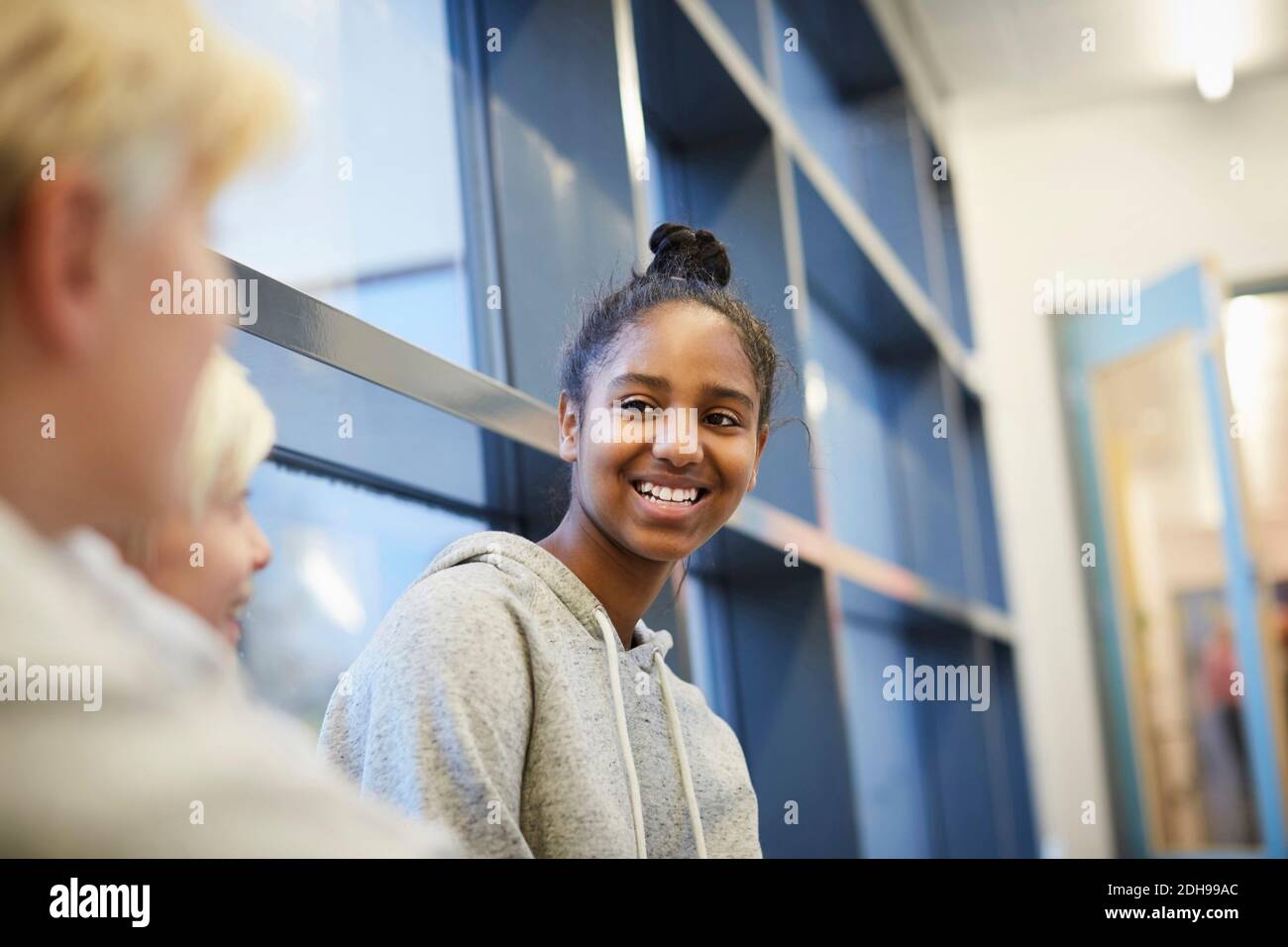 Lächelndes Mädchen der Mittelschule im Flur mit männlichen Freunden sprechen Stockfoto