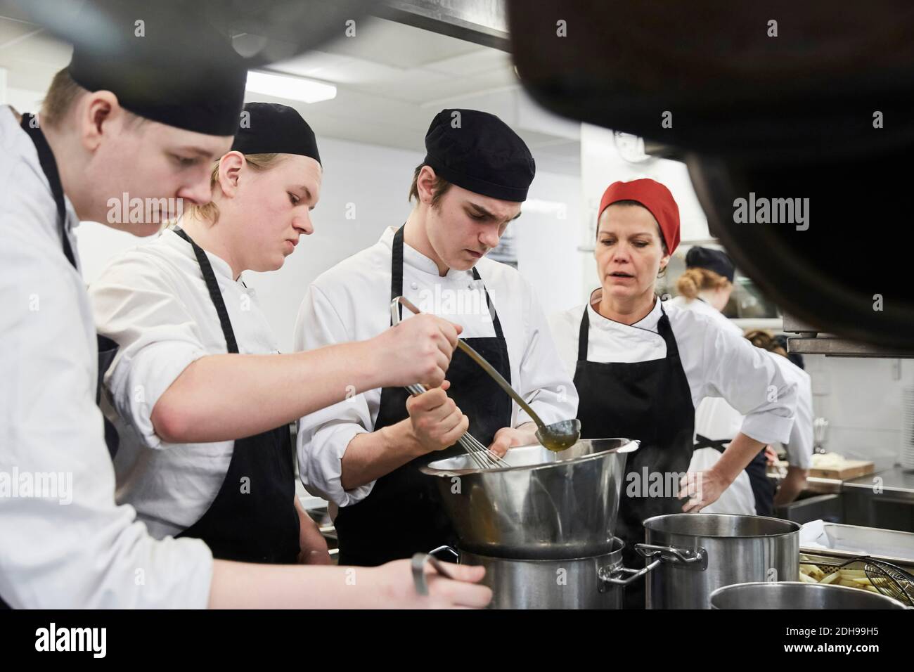 Lehrer, der männliche Schüler beim Kochen von Essen in der kommerziellen Küche unterstützt Stockfoto