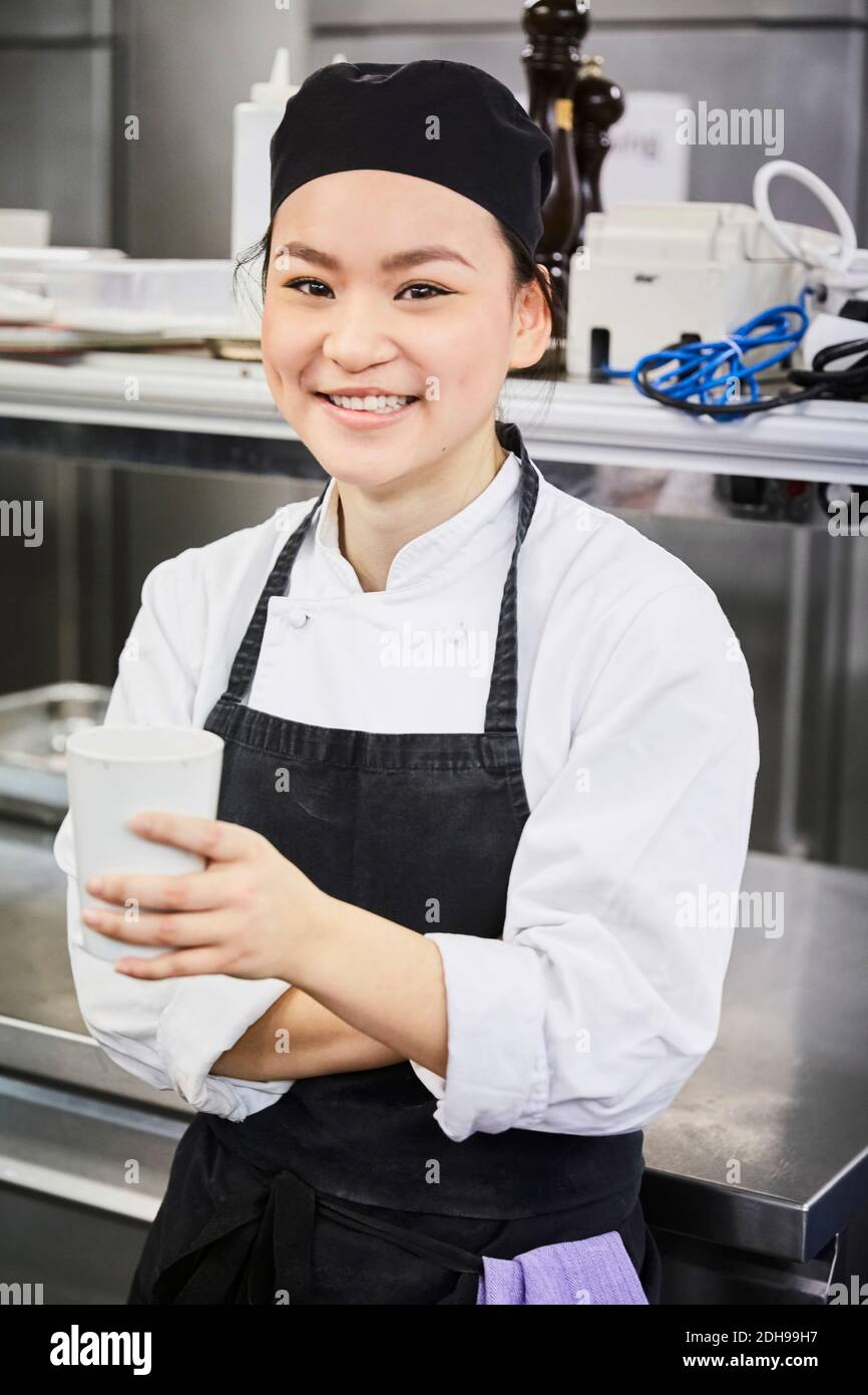 Portrait von lächelnden weiblichen Koch hält Einweg-Tasse in kommerziellen Küche Stockfoto