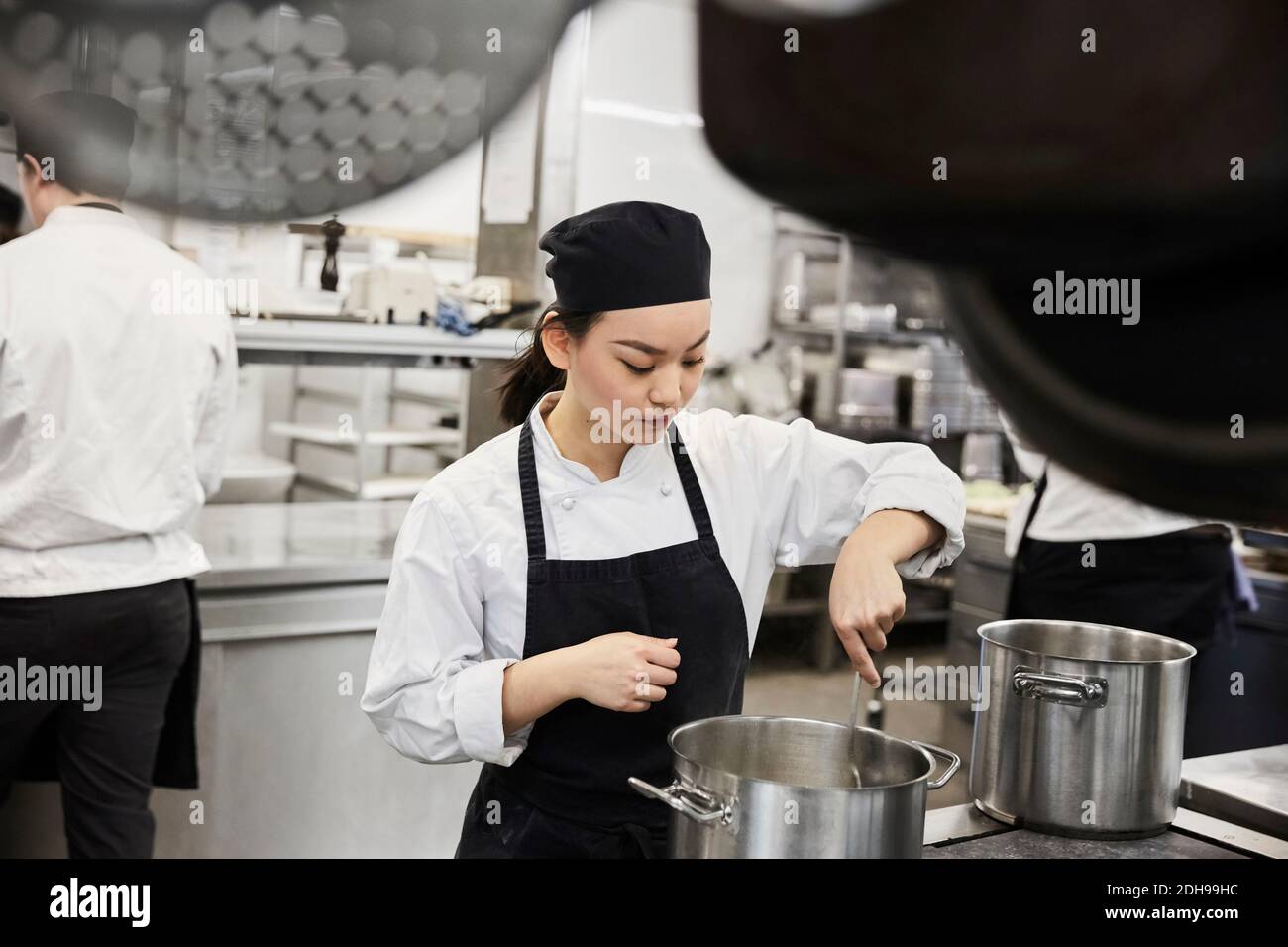 Junge weibliche Köchin, die Essen in der Kochpfanne bei Commercial rührt Küche Stockfoto
