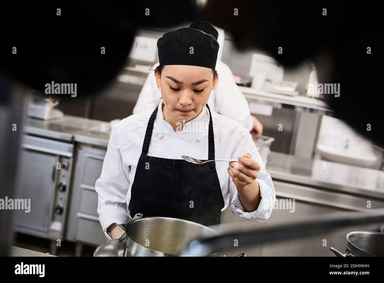 Junge weibliche Köchin, die Essen aus der Kochpfanne bei Commercial verkostet Küche Stockfoto