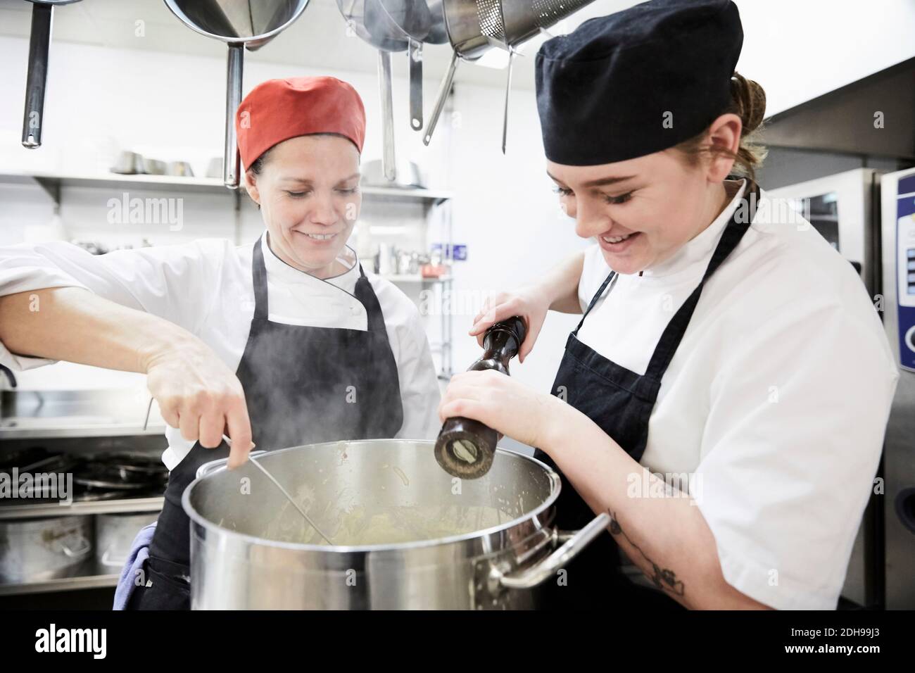 Lehrer mit weiblichen Schüler hinzufügen Pfeffer in die Pfanne an Gewerbliche Küche Stockfoto
