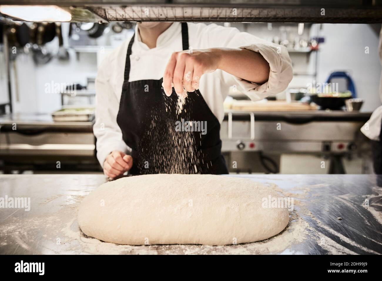 Mittelteil der weiblichen Chefstudentin bestreuen Mehl auf Teig an Gewerbliche Küche Stockfoto