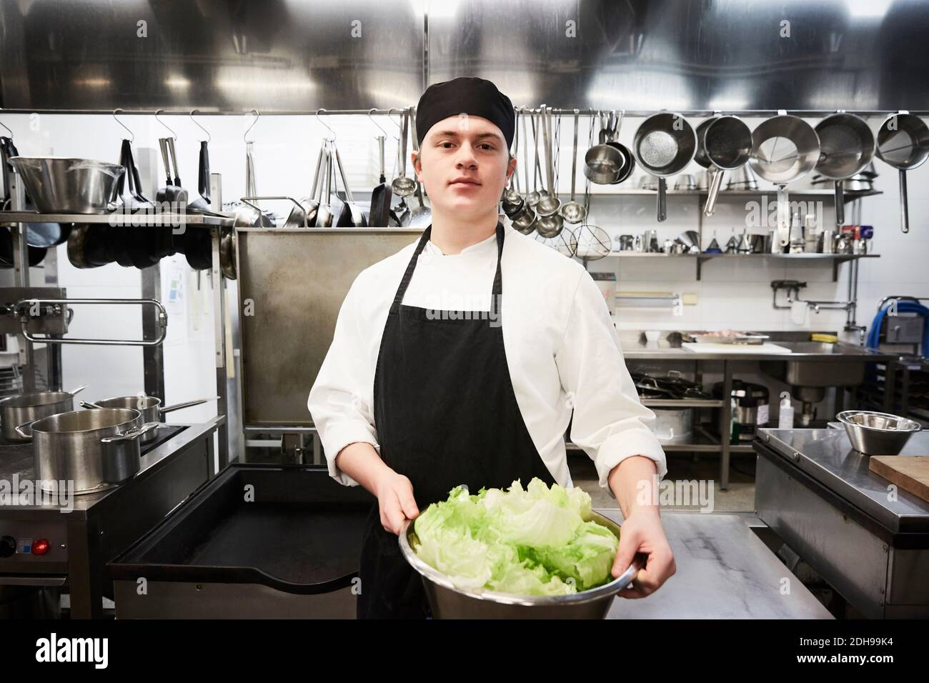 Portrait von selbstbewussten männlichen Chef hält Behälter mit Gemüse an Gewerbliche Küche Stockfoto