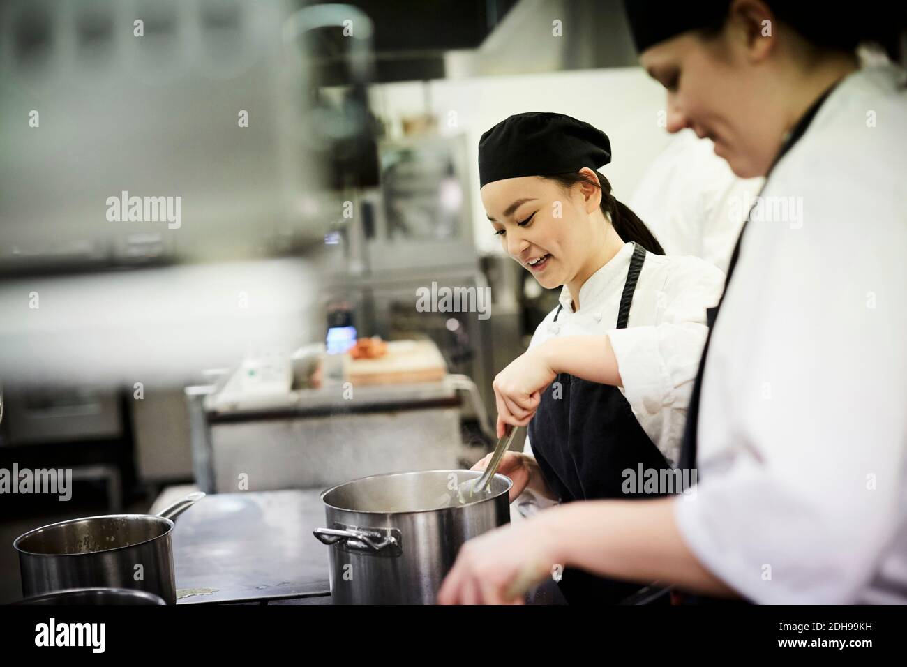 Weibliche Chefstudentin mit Kollegen, die Essen in der kommerziellen Küche kochen Stockfoto