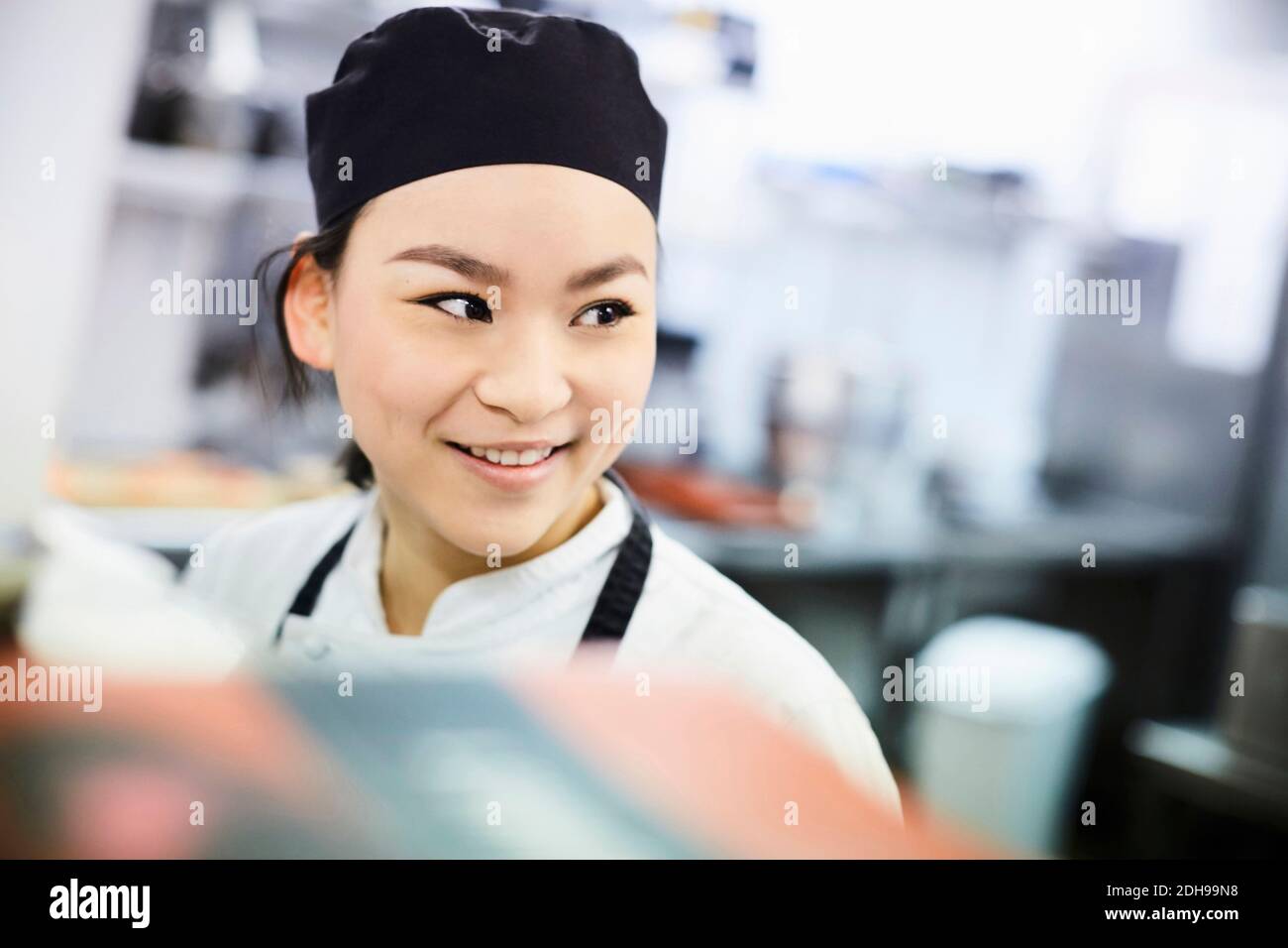 Lächelnde Köchin schaut weg in der kommerziellen Küche Stockfoto
