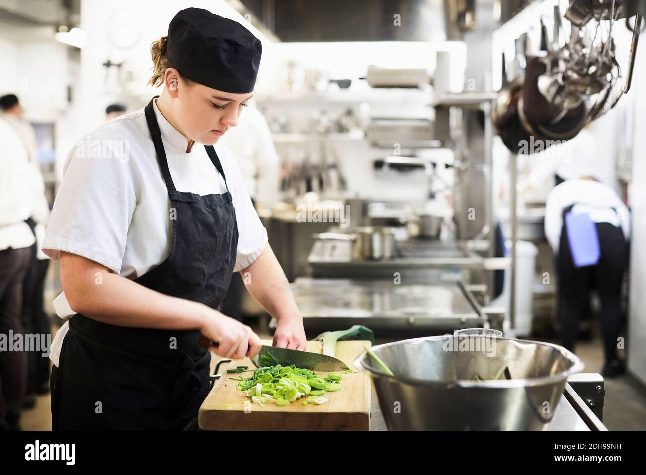 Junge Köchin hackt Gemüse auf Schneidebrett beim Kochen Schule Stockfoto