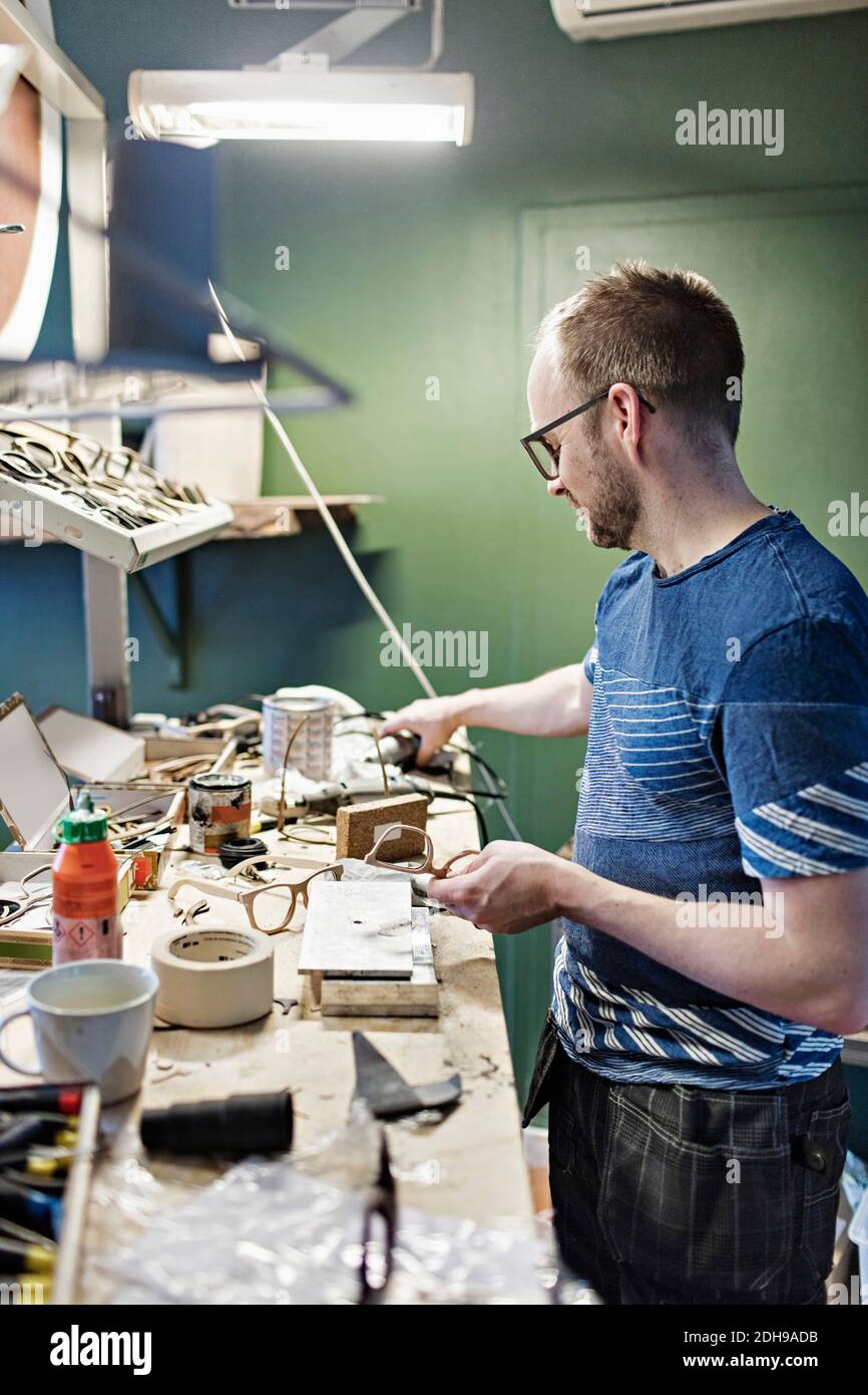Seitenansicht des männlichen Besitzers, der in der Brillenwerkstatt arbeitet Stockfoto