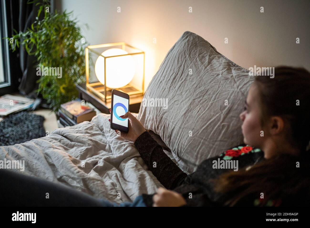 Teenager Mädchen Anpassung Beleuchtungsausrüstung durch Smartphone-App während Liegen im Schlafzimmer im Smart Home Stockfoto