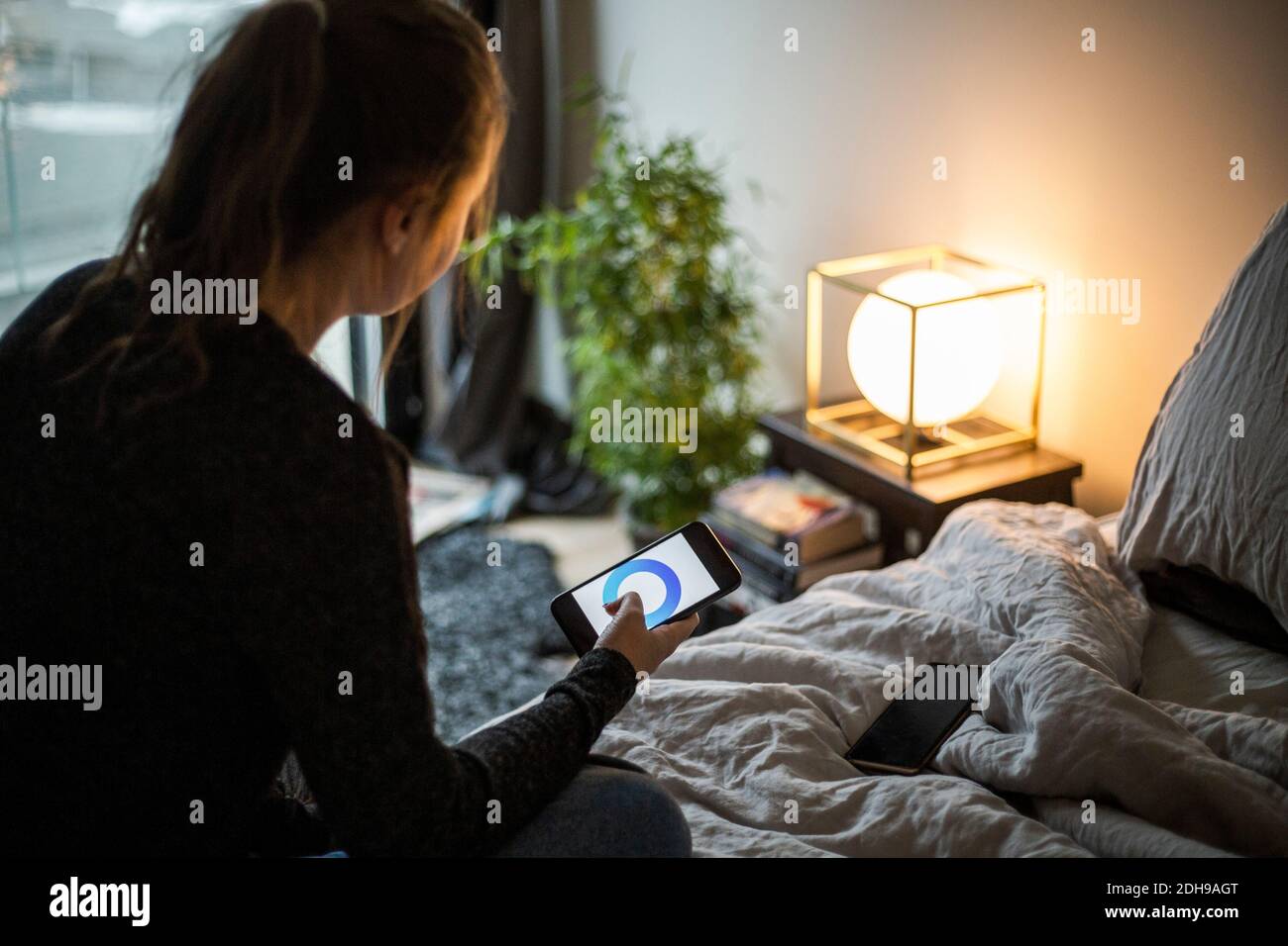 Teenager-Mädchen mit Smartphone-App, während die Anpassung der Beleuchtung Ausrüstung Im Schlafzimmer im Smart Home Stockfoto