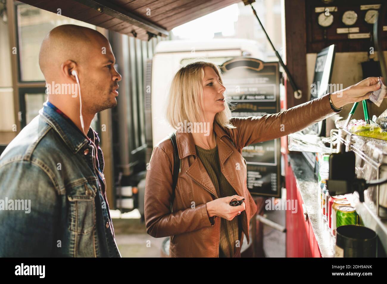 Mittelerwachsener Mann mit Frau, die Kaffee am Lebensmittelwagen kauft Stockfoto Mittelerwachsener Mann mit Frau, die Kaffee am Lebensmittelwagen kauft Stockfoto