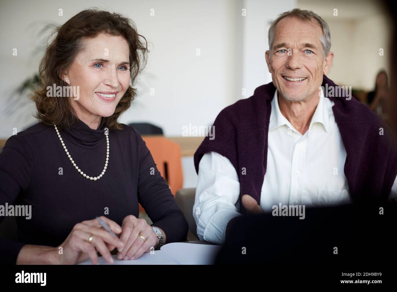 Lächelnde ältere Frau, die mit dem Mann während des Treffens beim Gesetz sitzt Fest Stockfoto