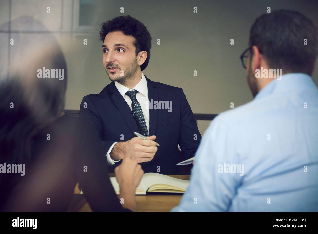 Junger männlicher Geschäftsmann sitzt mit Kollegen während der Sitzung bei Gesetz Fest Stockfoto