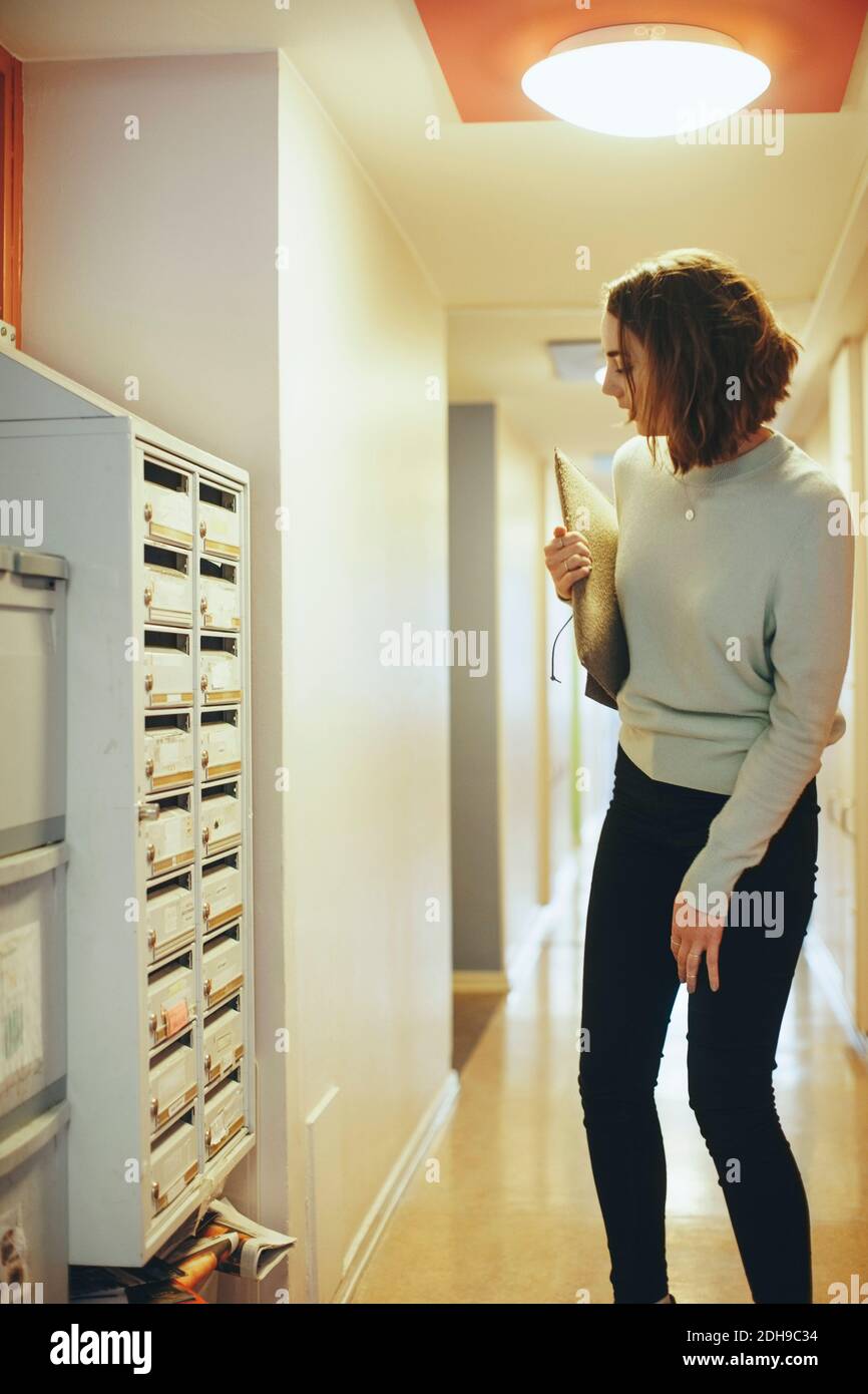 Frau hält Dokument Blick auf Briefkasten im Flur Stockfoto