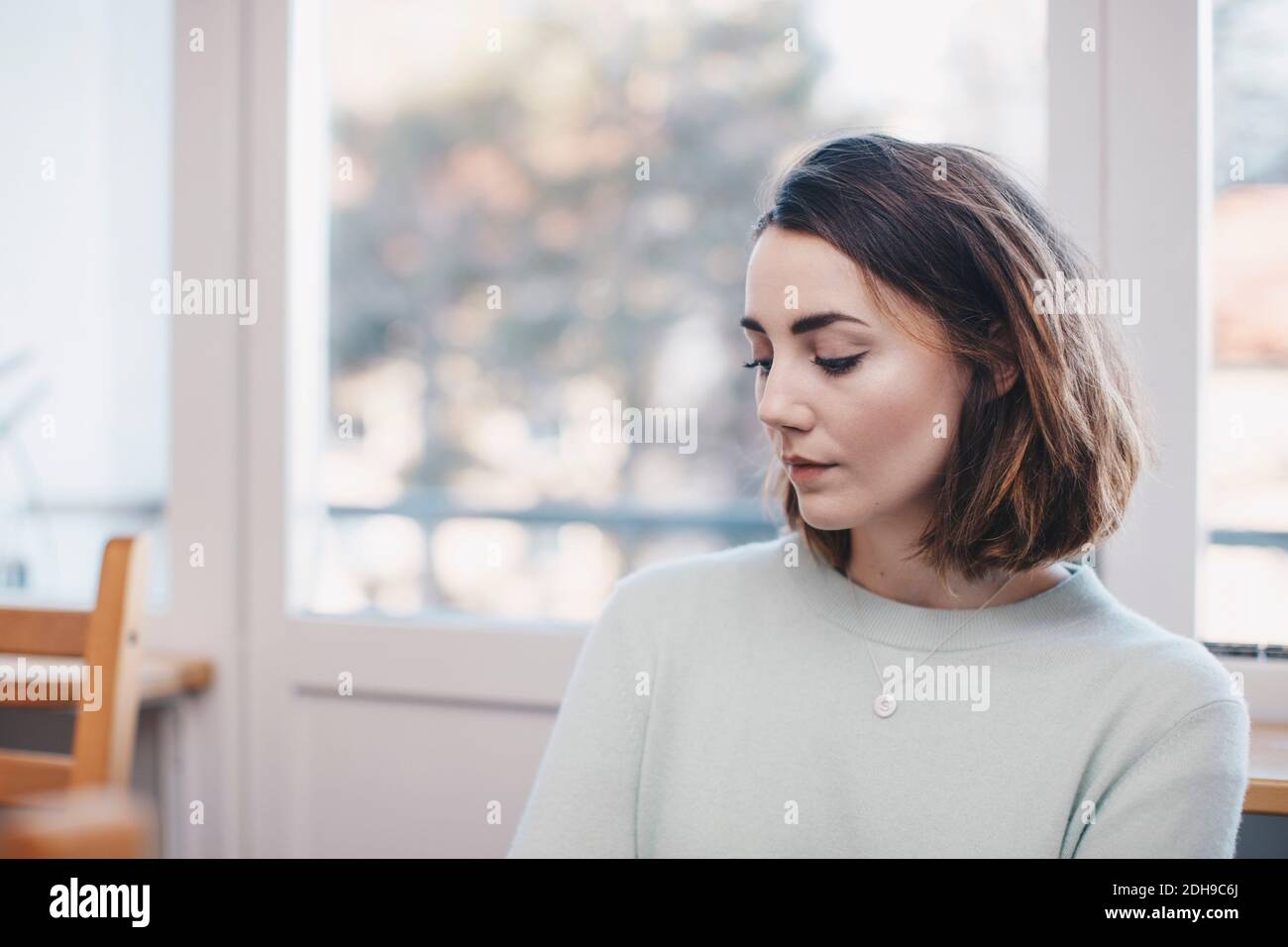 Frau, die im Studentenwohnheim gegen das Fenster sitzt Stockfoto