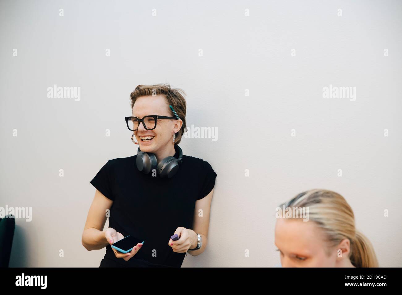 Lächelnder Genderblend-Business-Profi, der wegschaut, während er sich auf Weiß stützt Wand im beleuchteten Konferenzraum Stockfoto