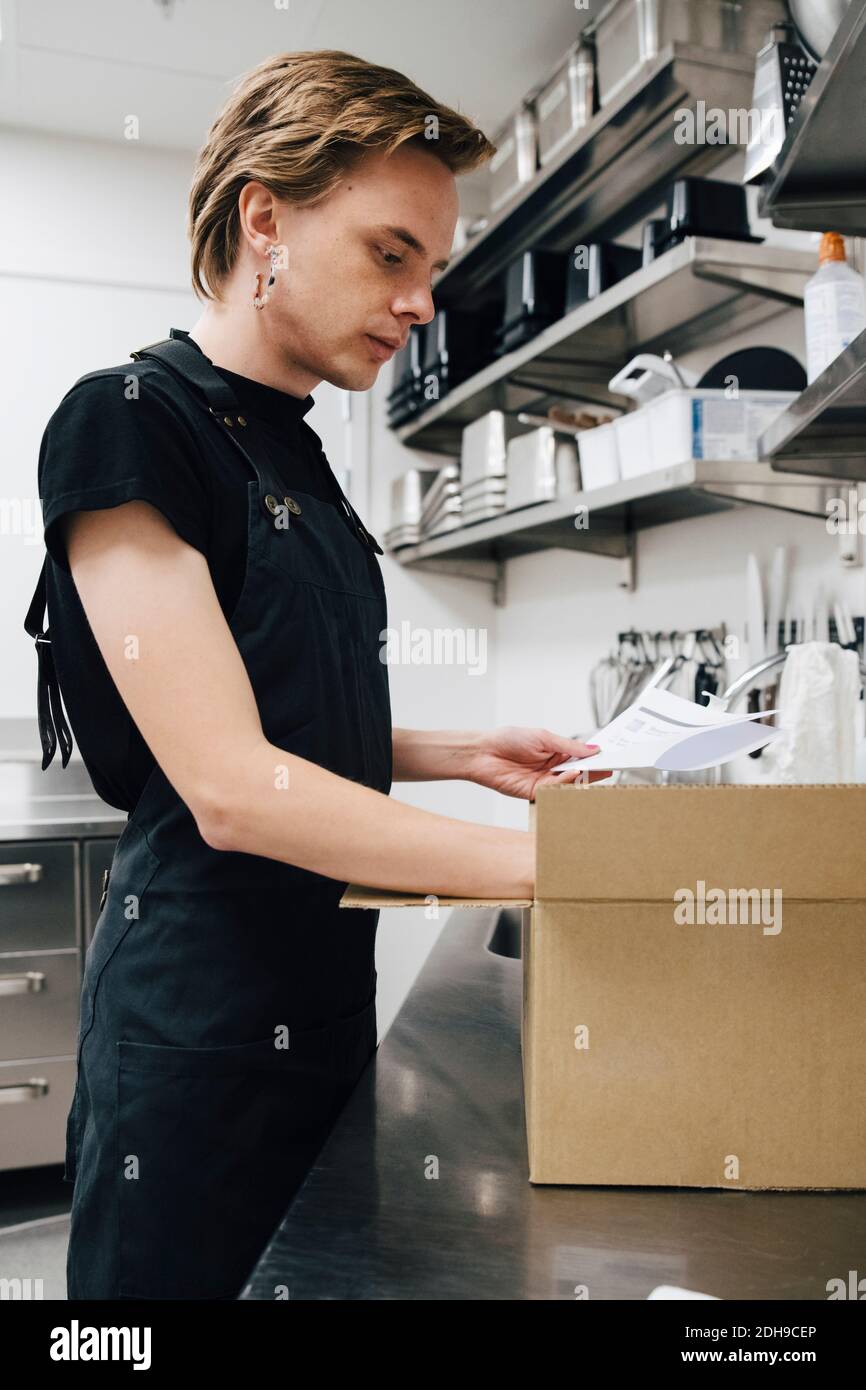 Seitenansicht der Liste der Barista-Holder für junge androgyne Barista nach Karton Box in der Café-Küche Stockfoto