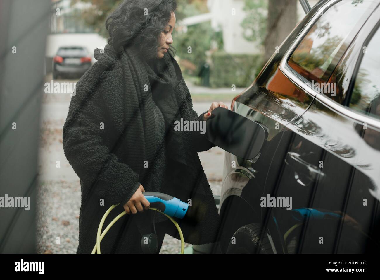 Mittlere Erwachsene Frau mit Elektroauto an der Ladestation gesehen Durch Glas Stockfoto