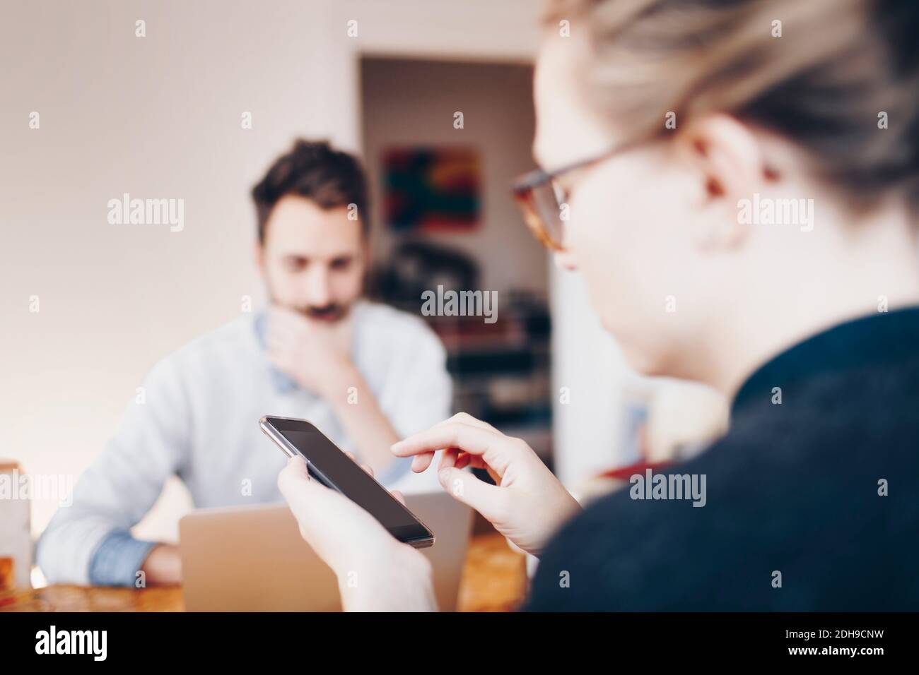 Frau mit Handy gegen Mann arbeiten auf Laptop an Zu Hause Stockfoto