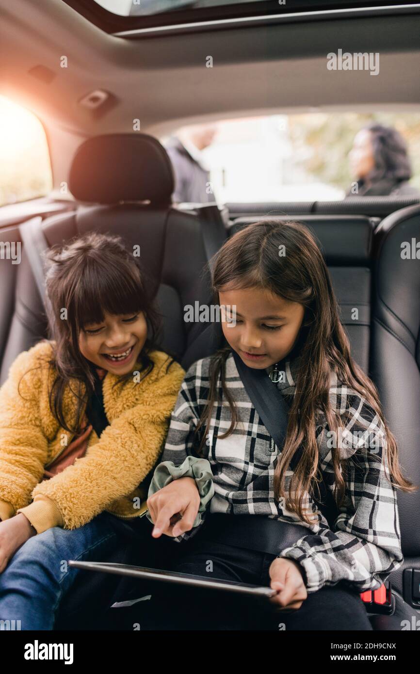 Schwestern, die im Auto sitzen und ein digitales Tablet nutzen Stockfoto