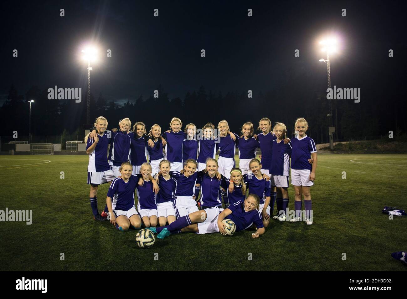 Porträt der Mädchen Fußballmannschaft auf beleuchteten Feld gegen Himmel Stockfoto