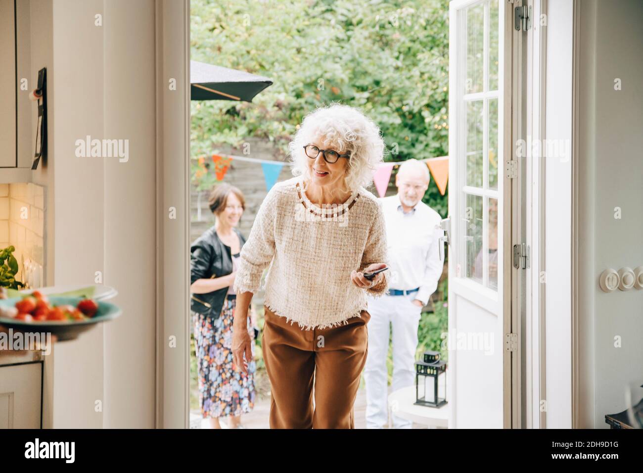 Lächelnde Frau mit lockigen weißen Haaren, die durch die Tür gegen Freunde Stockfoto