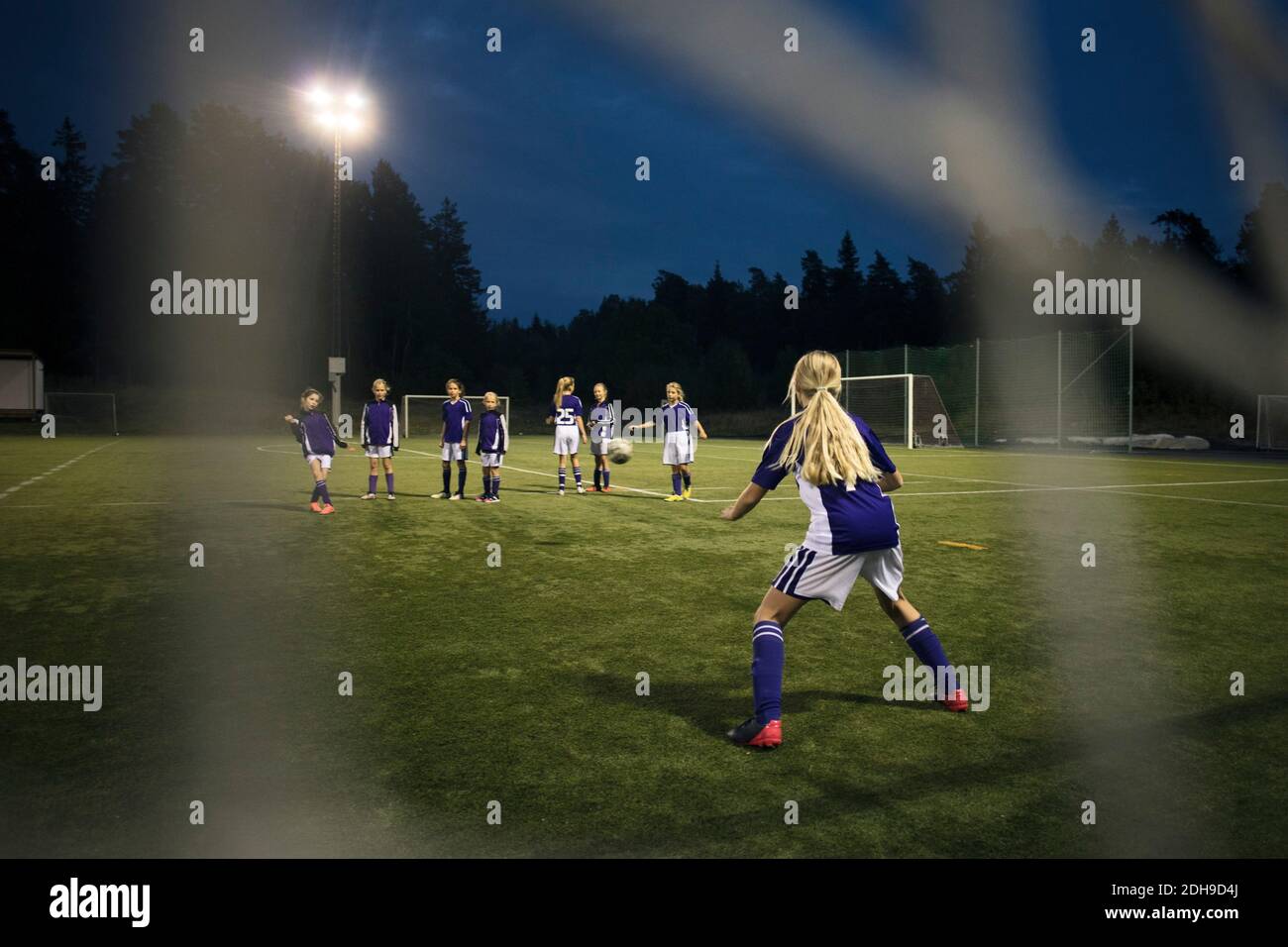 Mädchen, die Fußball spielen, gesehen vom Tor nach dem Netz auf dem Feld Gegen den Himmel Stockfoto