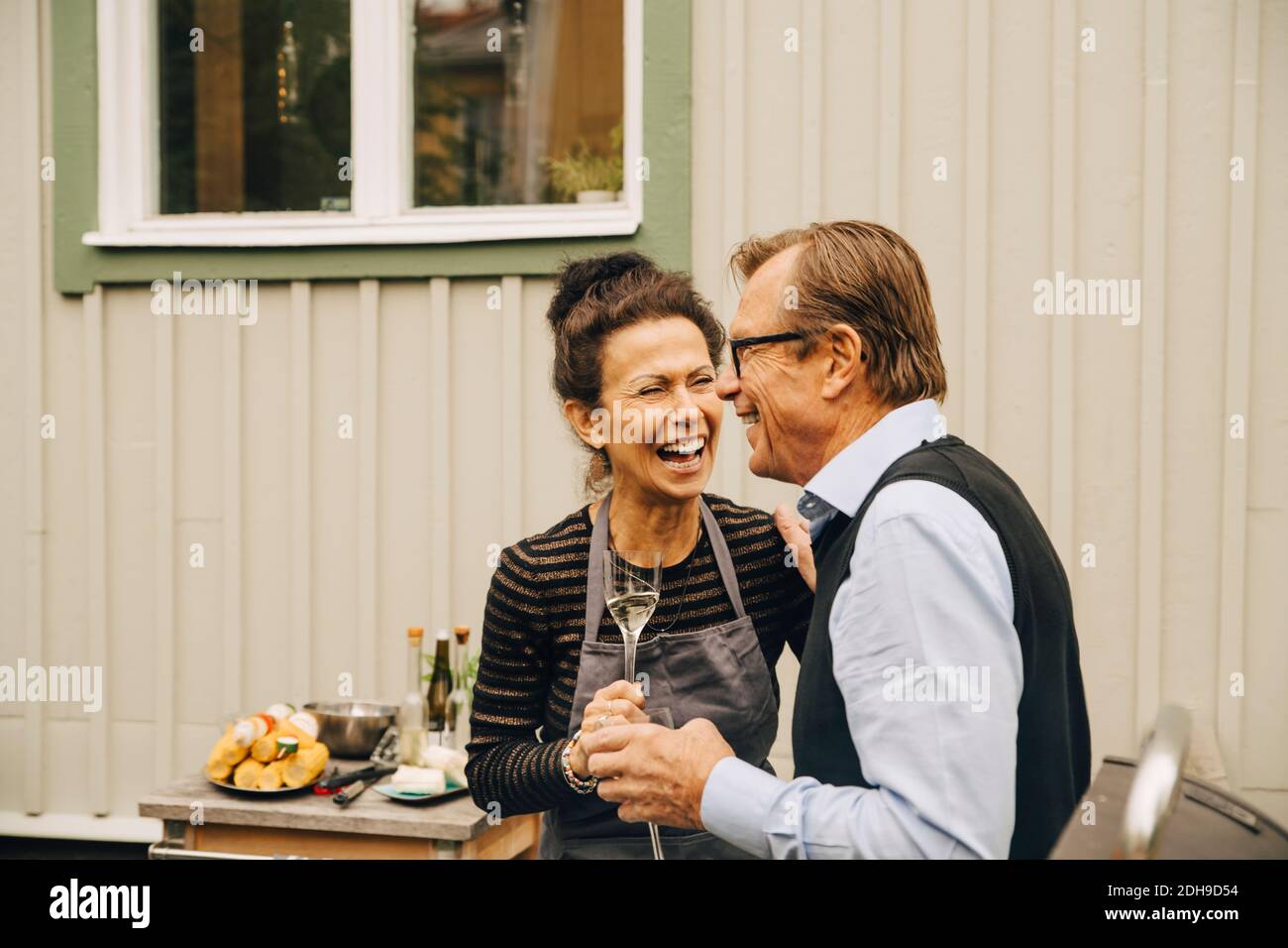 Ältere Männer und Frauen lachen, während sie das Getränk auf dem Rücken halten Hof während der Party Stockfoto