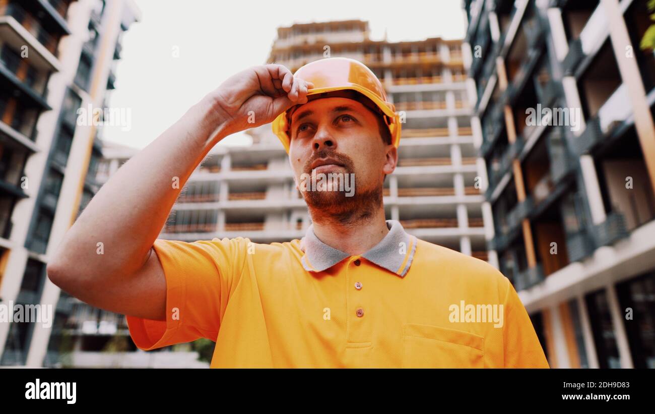 Bauarbeiter, der auf der Baustelle seinen Schutzhelm aufsetzt. Sicherheit geht vor, Berufskonzept. Der Baumeister legt einen Hut an Stockfoto