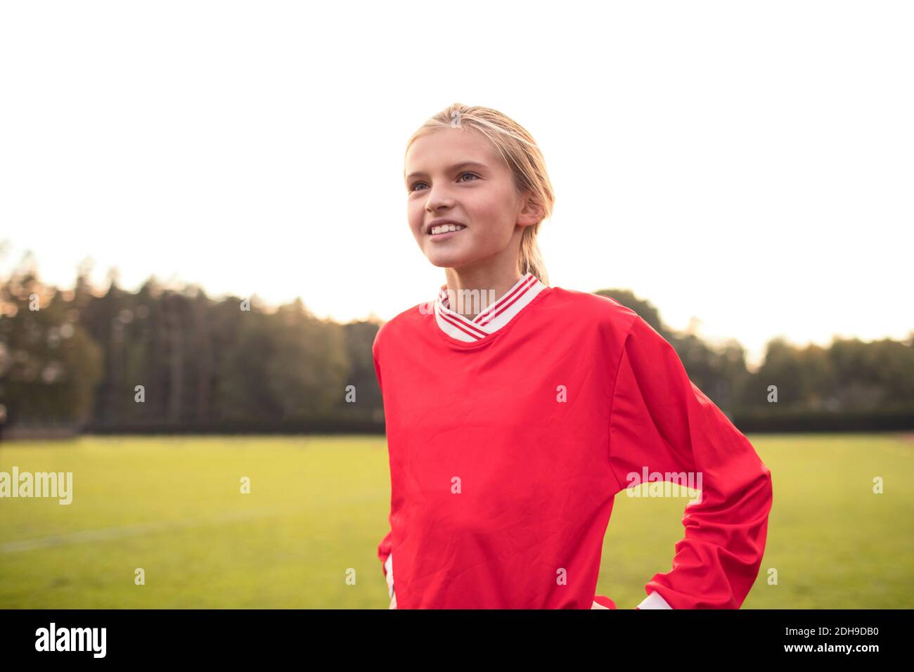 Glückliche weibliche Fußballspielerin schaut weg stehen auf dem Feld gegen Himmel Stockfoto