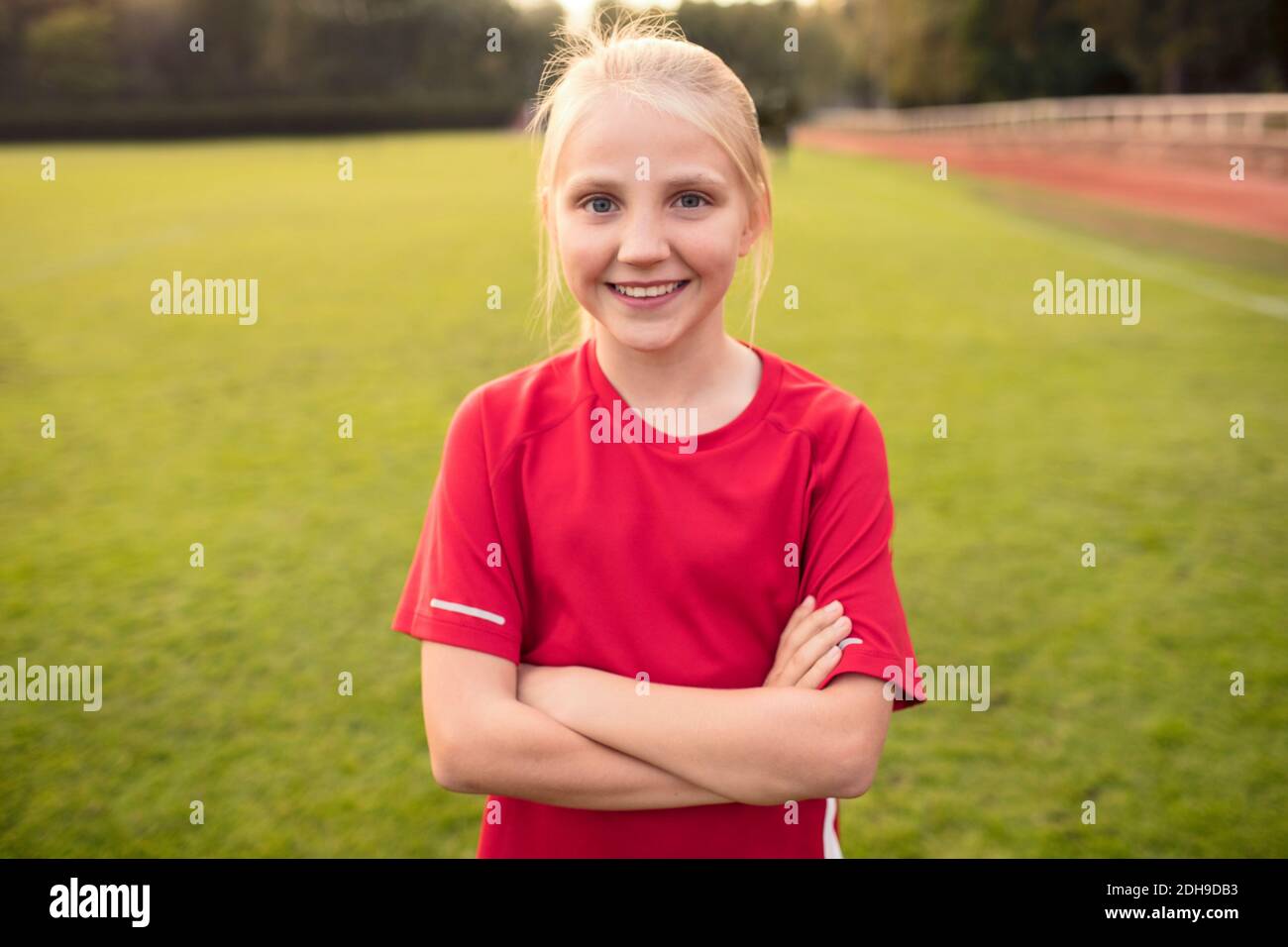 Portrait von glücklichen Mädchen trägt rote T-Shirt stehen mit Armen Gekreuzt auf dem Fußballplatz Stockfoto