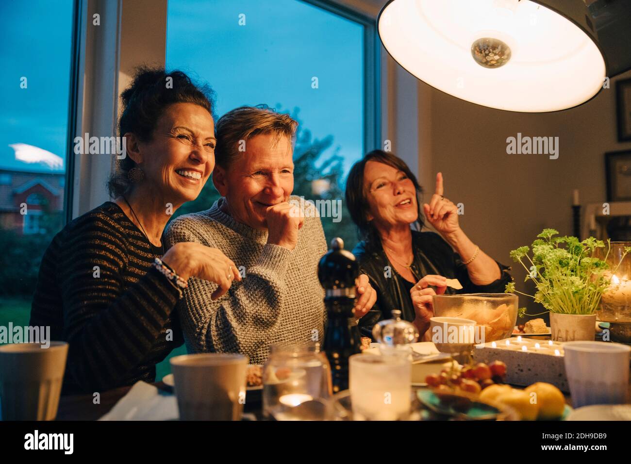 Glückliche ältere Frauen und Mann sitzen am beleuchteten Esstisch Beim Abendessen Party genießen Stockfoto