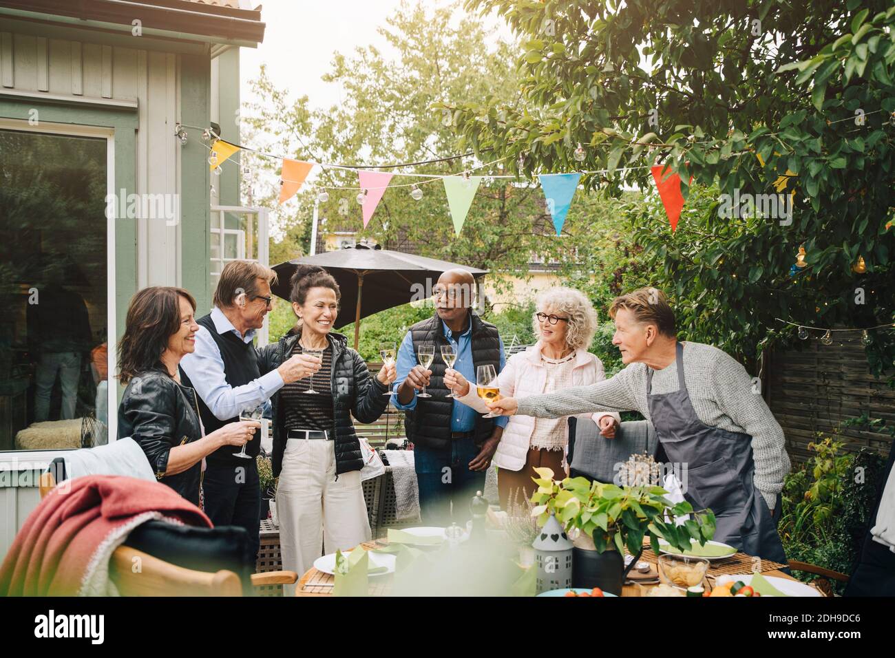 Aktive ältere männliche und weibliche Freunde, die Toast mit Getränk anstoßen Während des Stehens im Hinterhof während der Garten-Dinner-Party Stockfoto