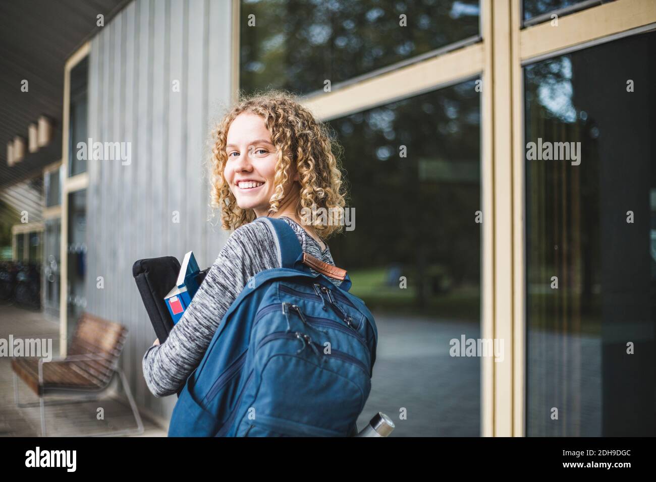 Porträt einer lächelnden jungen Frau mit Tasche auf dem Universitätscampus Stockfoto